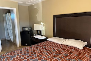 Habitación de hotel con cama, mesita de noche, lámpara, televisión y puerta de baño.