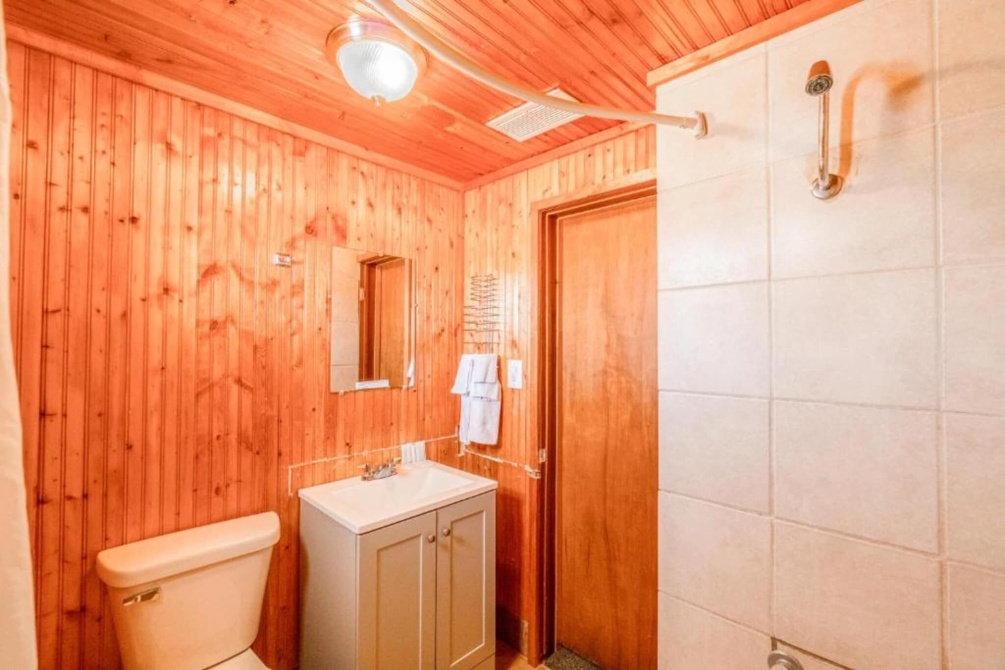 A wooden-paneled bathroom with a toilet, sink, mirror, and shower.