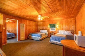 Quarto de cabana de madeira com duas camas, um ventilador de teto, micro-ondas e uma porta que dá para outro cômodo.