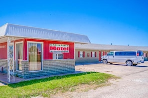 Um motel com fachada vermelha e branca, uma área de estacionamento e uma van branca estacionada na frente.