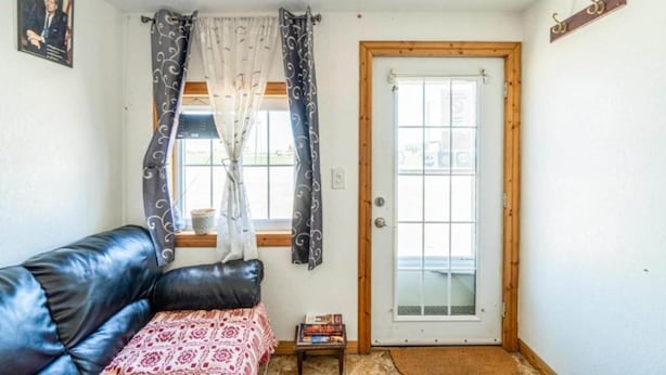 A room with a black leather sofa, a small table with books, a door with a glass panel, and a window with curtains.