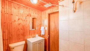 Un baño con paneles de madera, que incluye un inodoro, lavamanos, espejo y ducha.