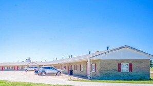 Un motel con varias habitaciones, un estacionamiento y un pequeño edificio con contraventanas rojas.