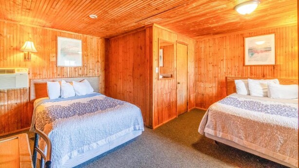Una habitación con paneles de madera, dos camas, una puerta y un cuadro en la pared.