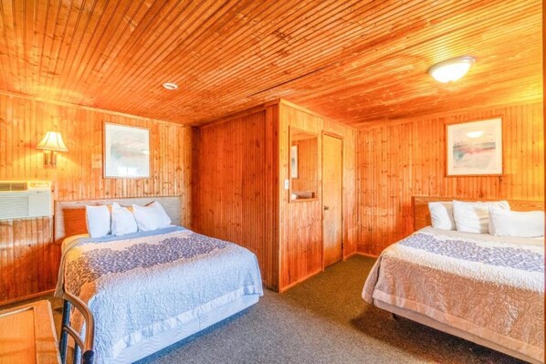 Una habitación con paneles de madera, dos camas, una puerta y un cuadro en la pared.
