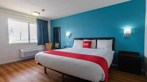 A hotel room with a bed, a window, a heater, and a nightstand.