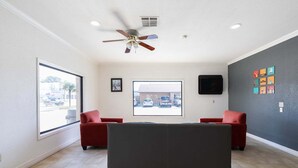 A room with a ceiling fan, a large window, a television, and a red couch.