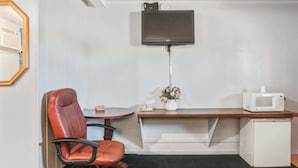 A small room with a desk, chair, TV, microwave, and a small refrigerator.