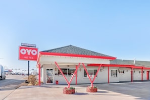 Un hôtel OYO d’époque, avec une façade rouge et blanche, un parking couvert et un ciel d’un bleu limpide.