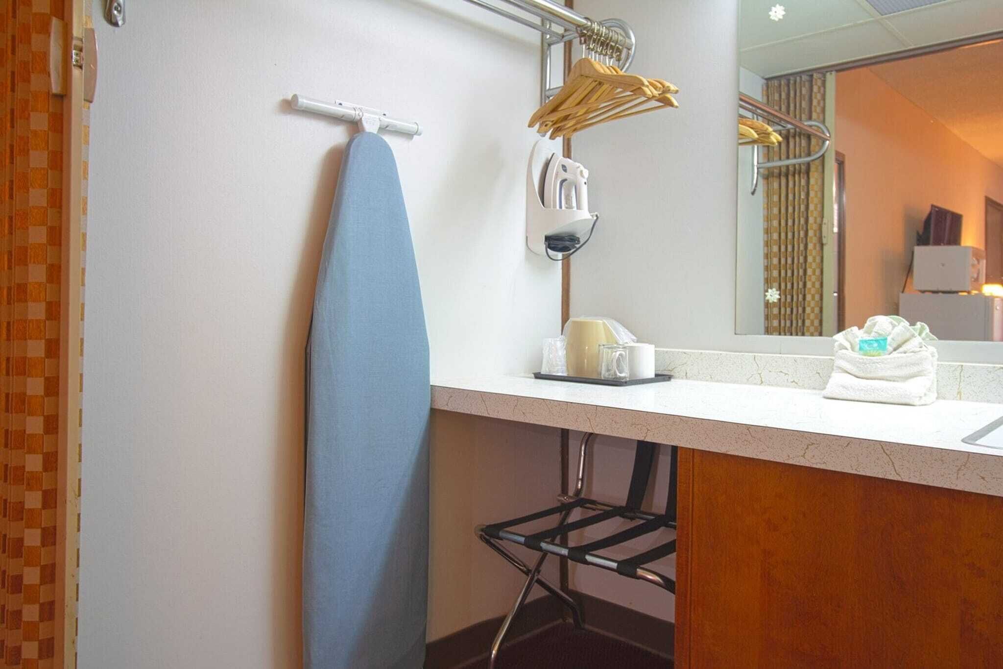 Baño de hotel con lavamanos, espejo, toallero y tabla de planchar, además de otro toallero con toallas dobladas.