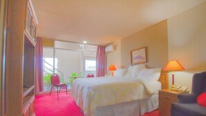 A hotel room with a large bed, two bedside lamps, a desk with a telephone, and a chair.