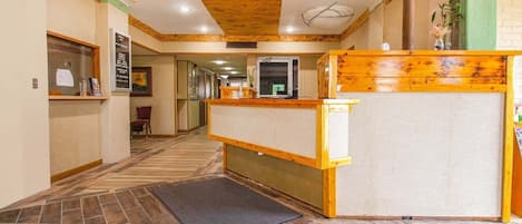 Un vestíbulo de hotel con un mostrador de recepción de madera, una zona de recepción y un piso de baldosas.