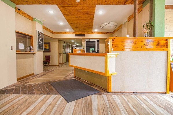 Un hall d’hôtel avec un comptoir d’accueil en bois, un espace de réception et un sol carrelé.