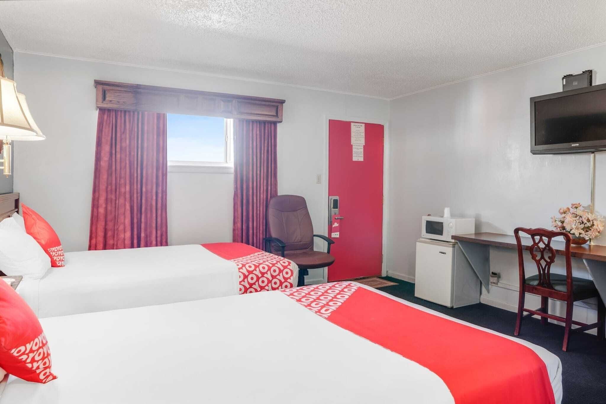 Une chambre d’hôtel avec deux lits, un bureau, une chaise, une télévision et un petit réfrigérateur.