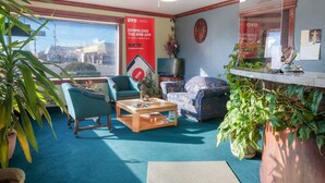 Een hotelkamer met een groot raam, een plafondventilator, een bank, een bijzettafeltje en diverse kamerplanten.