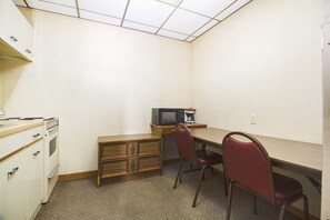 A small kitchenette with a microwave, coffee maker, and oven. There is a wooden desk with a chair and a small drawer unit.
