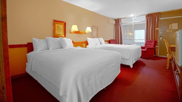 Ein Hotelzimmer mit zwei Betten, einem roten Teppich, einem roten Sessel und einem Fenster mit Vorhängen.