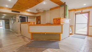 Ein Empfangsbereich mit Holztresen, einer Fußmatte am Eingang und einem Flur mit Holzböden.