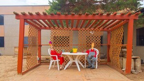 Ein überdachter Patio-Bereich mit einer Holz-Pergola, einem weißen Tisch und zwei Stühlen.