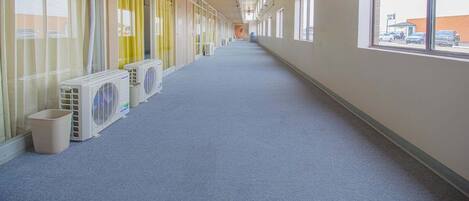 A long hallway with air conditioning units, large windows, and a carpeted floor.