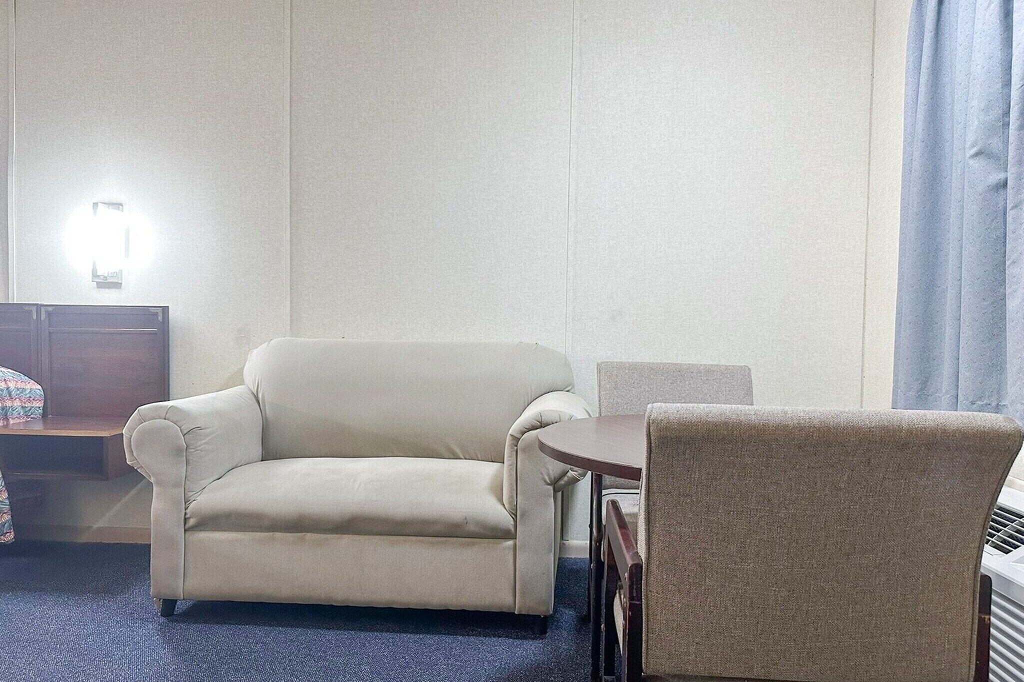 Hotelkamer met een beige bank, een ronde tafel, een stoel, een klein bureau en een wandlamp.