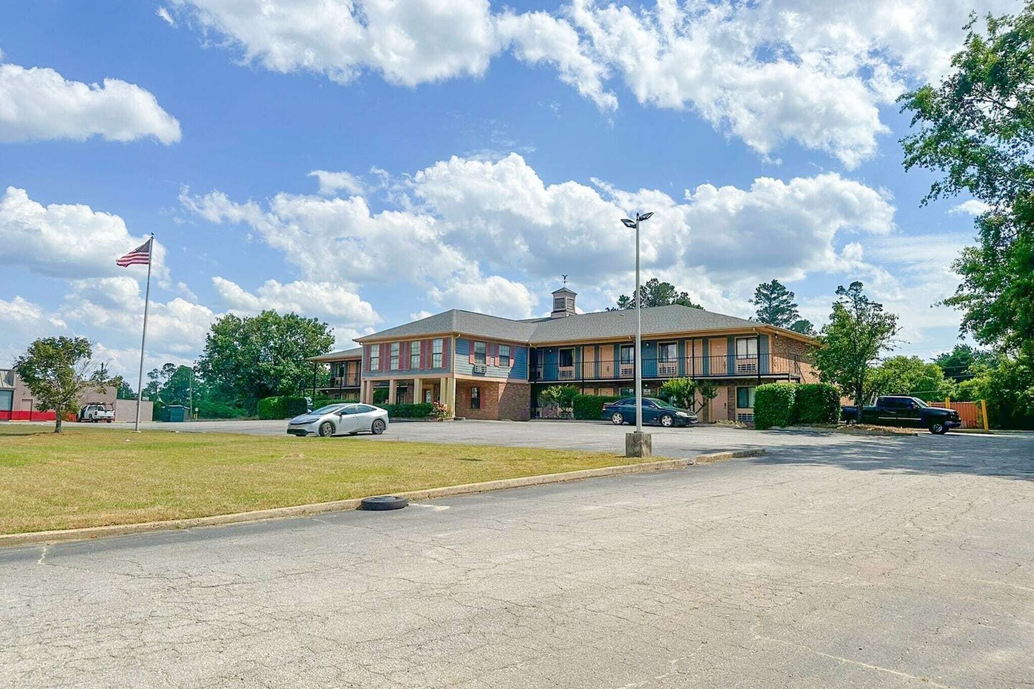 A two-story building with a flat roof, a flagpole with an American flag, and a parking lot with several cars.