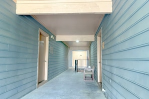 A narrow hallway with doors on both sides, a small table with chairs, and a railing in the distance.