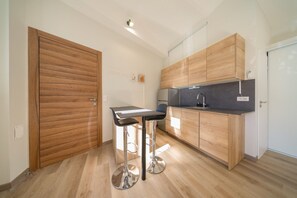 Eine kleine Küche mit Holzschränken, einem Edelstahlkühlschrank und einem Barhocker.