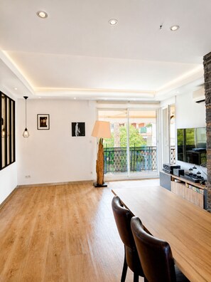 A spacious living area with a wooden floor, a dining table with chairs, a TV, and a balcony with a view. - 225 Le Club C in Cannes (Cannes)