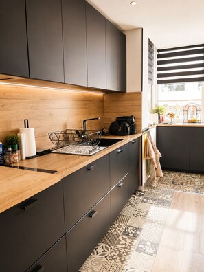A modern kitchen with dark cabinets, a wooden countertop, and a patterned tile floor. - 225 Le Club C in Cannes (Cannes)