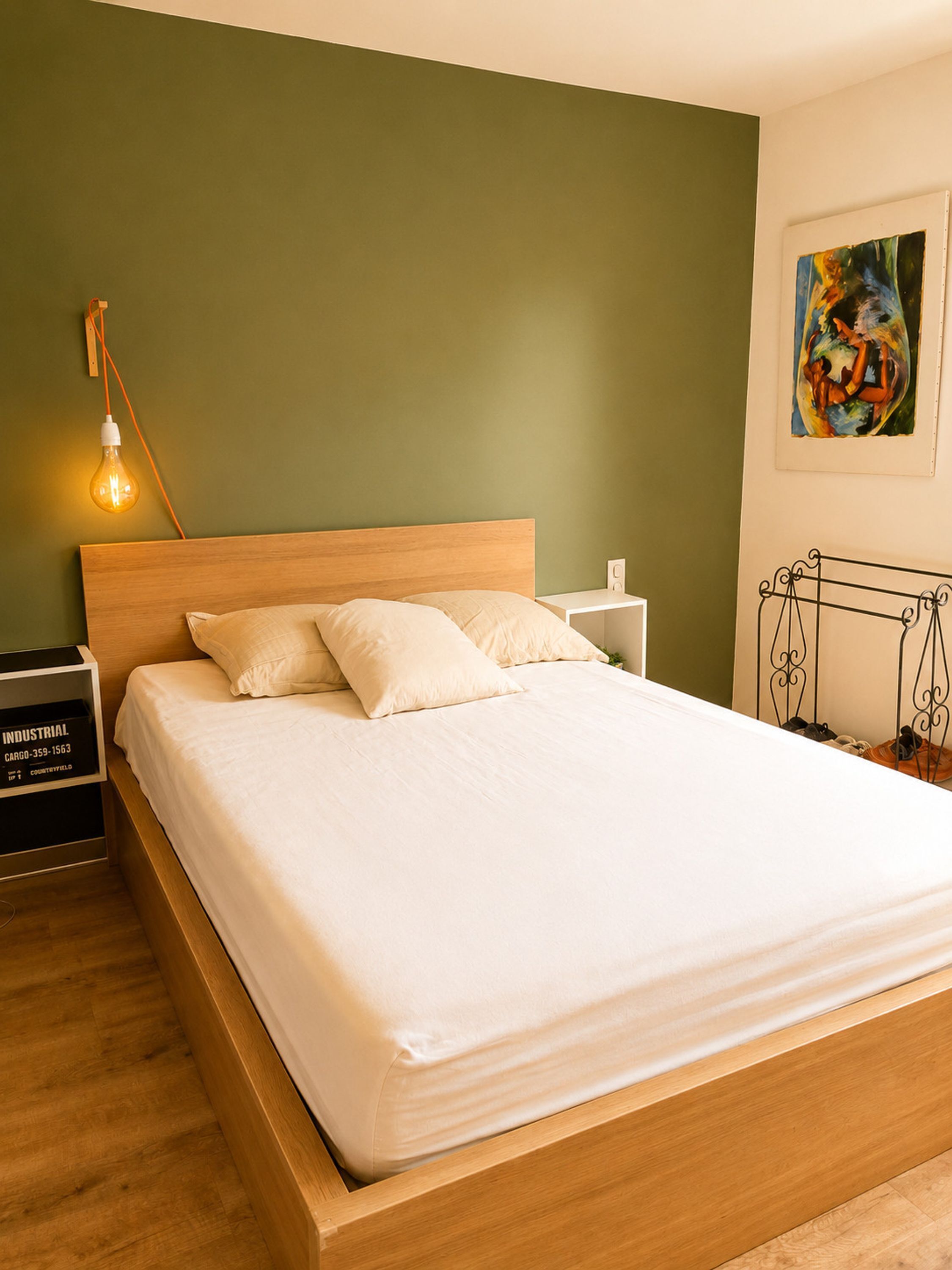 A neatly made bed with a wooden headboard, a bedside table with a lamp, and a painting on the wall.