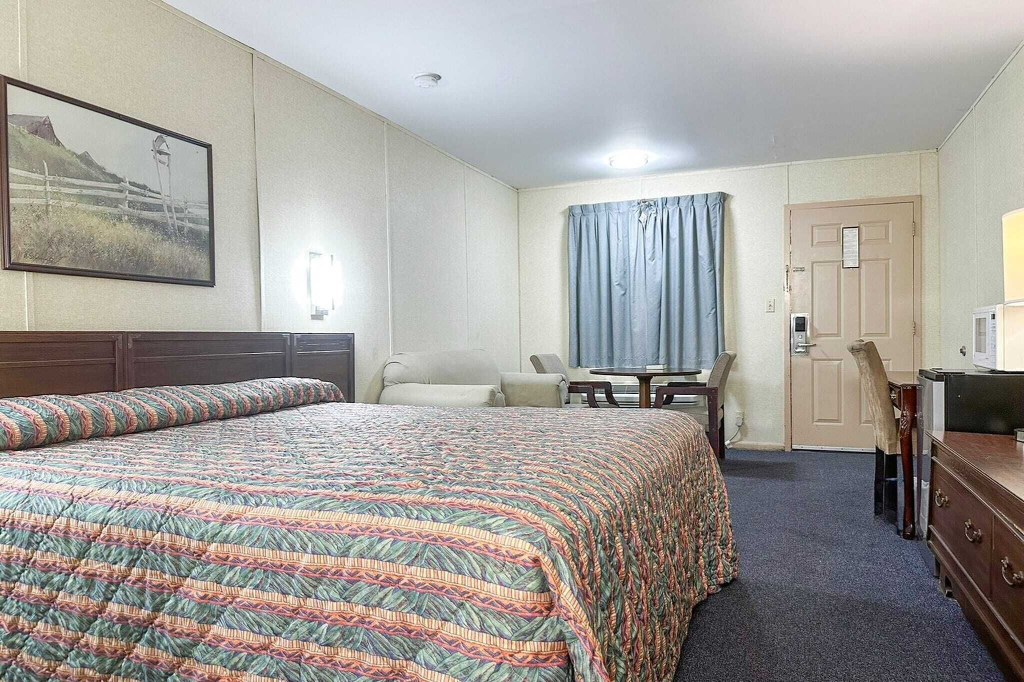 A hotel room with a large bed, a desk, a chair, a dresser, and a door.