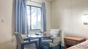 A hotel room with a bed, a desk, a chair, a small table, and a window with curtains. - Louisville, GA|King Bed|Smoking (Louisville, GA)