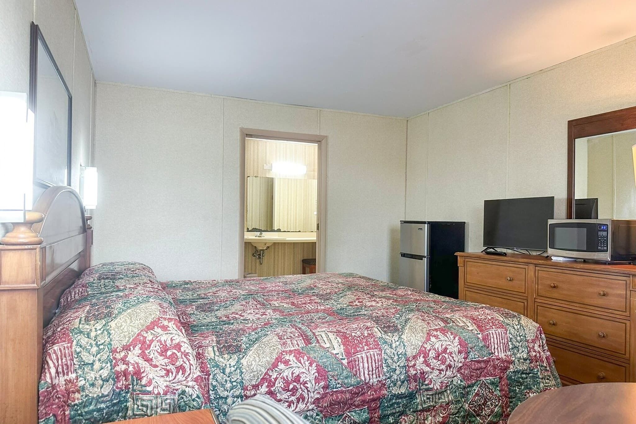 Een hotelkamer met een bed, een dressoir, een televisie, een magnetron en een spiegel.