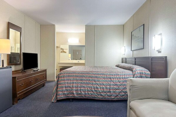 Une chambre d’hôtel avec un lit, une commode, une télévision, un miroir et un tableau encadré au mur.