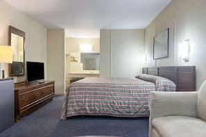 A hotel room with a bed, a dresser, a television, a mirror, and a framed picture on the wall.