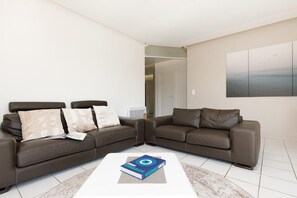 Ein modernes Wohnzimmer mit zwei braunen Ledersofas, einem weißen Couchtisch mit einem Buch und einem großen abstrakten Gemälde an der Wand.