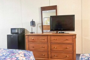 A hotel room with a wooden dresser, a television, a microwave, a lamp, and a bed with floral bedding.