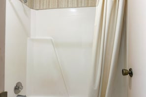 Una banyera blanca amb cortina de dutxa, un mànec metàl·lic i un angle amb paret amb textura.