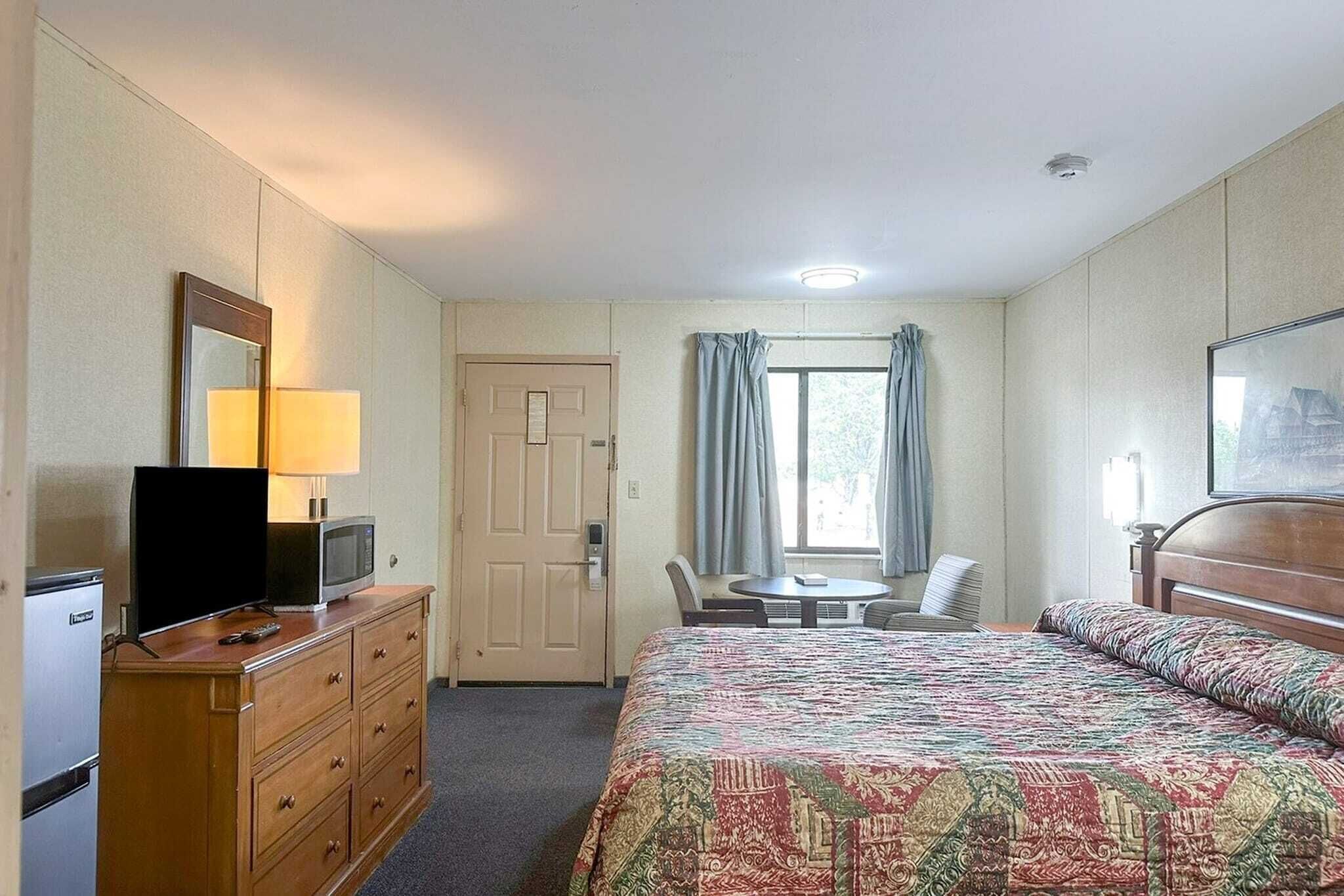 A hotel room with a bed, a desk with a chair, a television, a dresser, and a window with curtains.