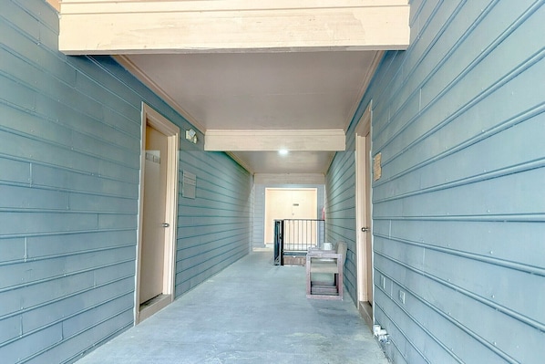 A narrow hallway with doors on both sides, a small table with chairs, and a railing in the distance.