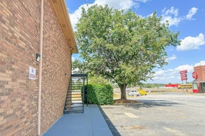 A brick building with a 'NO LOITERING' sign, a tree, and a parking lot with a yellow vehicle.