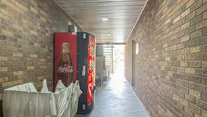 Un couloir aux murs de briques, un distributeur automatique de Coca-Cola et un espace abrité recouvert d’un tissu blanc.