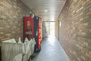 A corridor with brick walls, a Coca-Cola vending machine, and a covered area with white fabric.