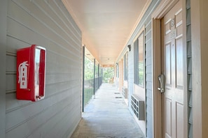 A corridor with a fire extinguisher on the left, a door on the right, and a bench in the distance.