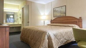 Une chambre d’hôtel avec un lit, un bureau, une chaise, un miroir et une lampe.