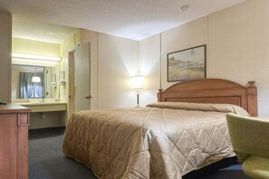 A hotel room with a bed, a desk, a chair, a mirror, and a lamp.