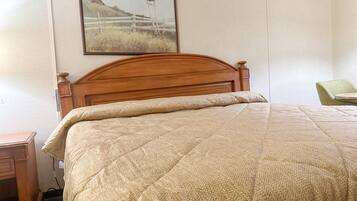 A bedroom with a wooden headboard, a beige quilted bedspread, a nightstand, and a framed picture on the wall.