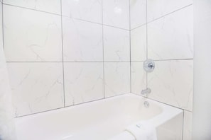 Een badkamer met witte marmeren tegels, een bad en een douchekop.