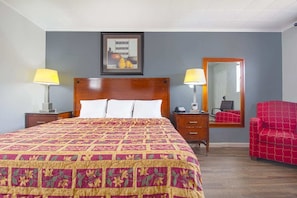 A hotel room with a large bed, two bedside tables, a red armchair, a mirror, and a framed picture on the wall.